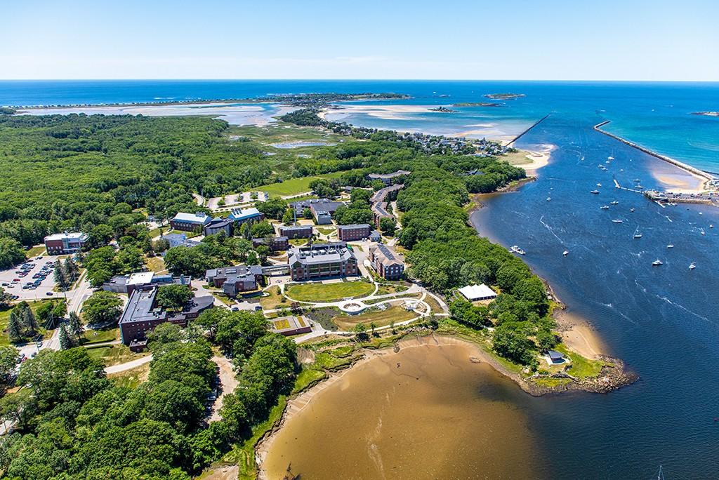 An aerial view of the Biddeford Campus showing campus buildings, nearby forest, beach, river, and the ocean