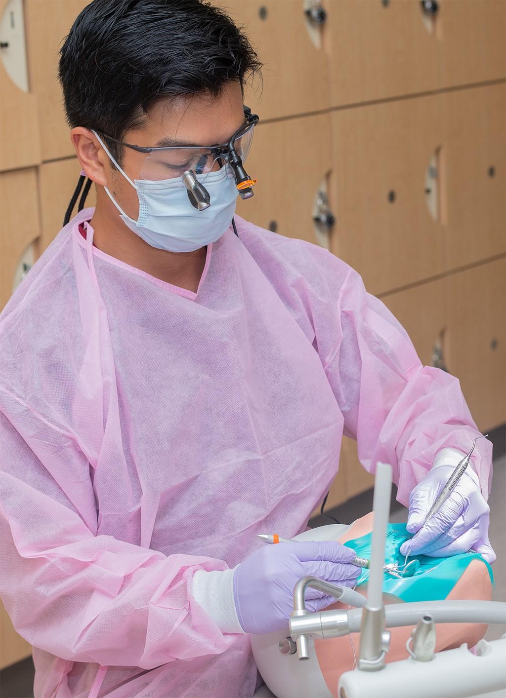 一名穿着粉色磨砂服的牙科医学院学生在口腔健康中心练习技能