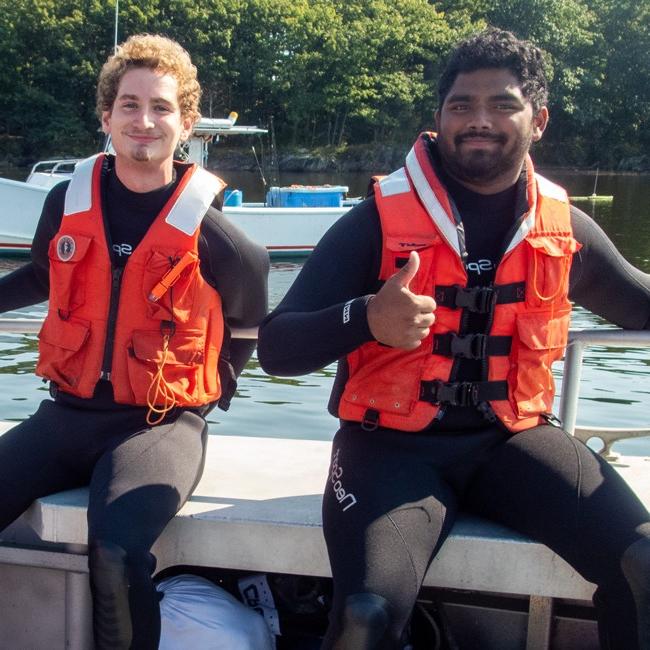 两名身穿救生衣的学生坐在欧盟船上的长凳上微笑着