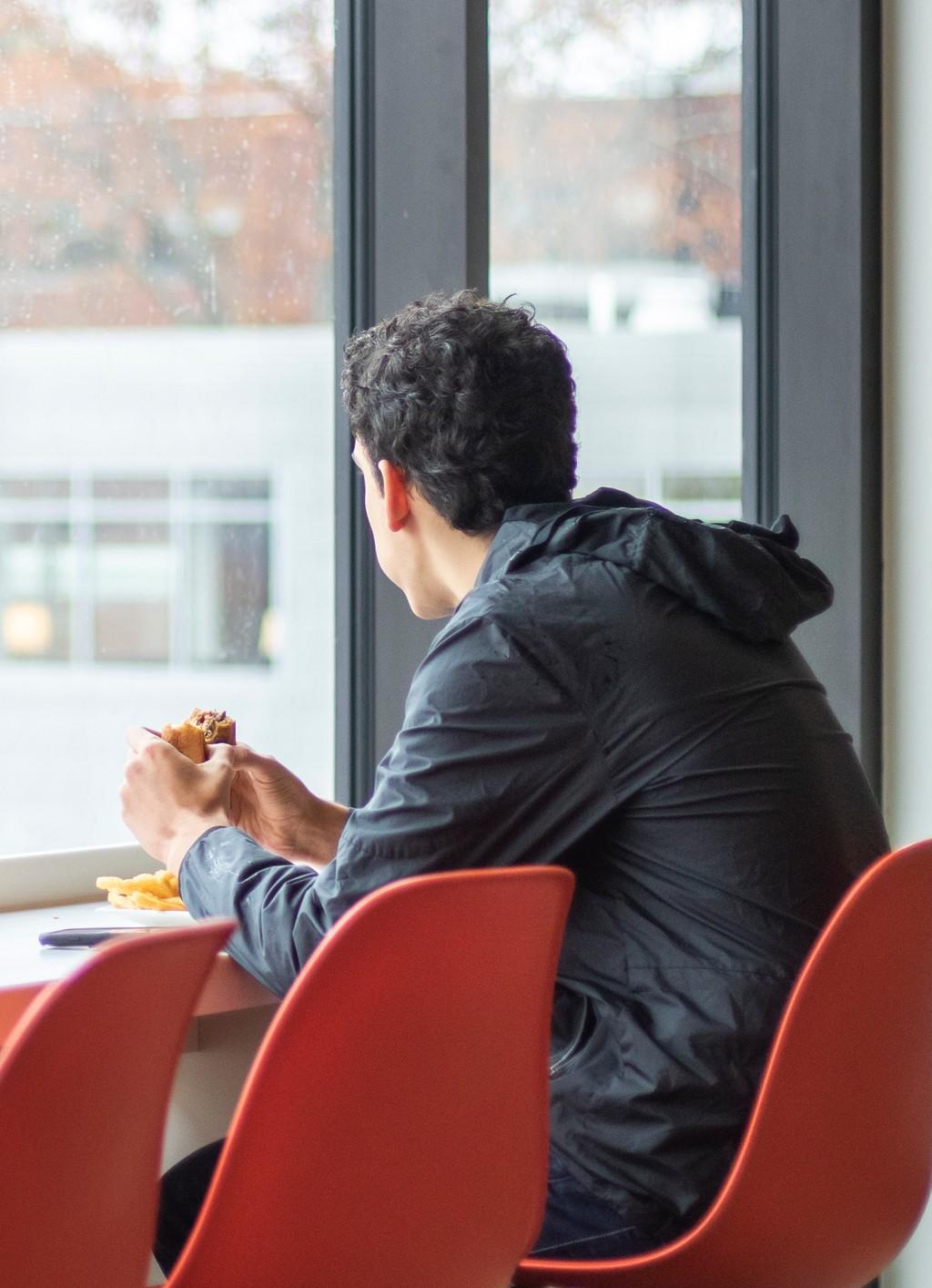 A student eating a hamburger while looking out large glass windows