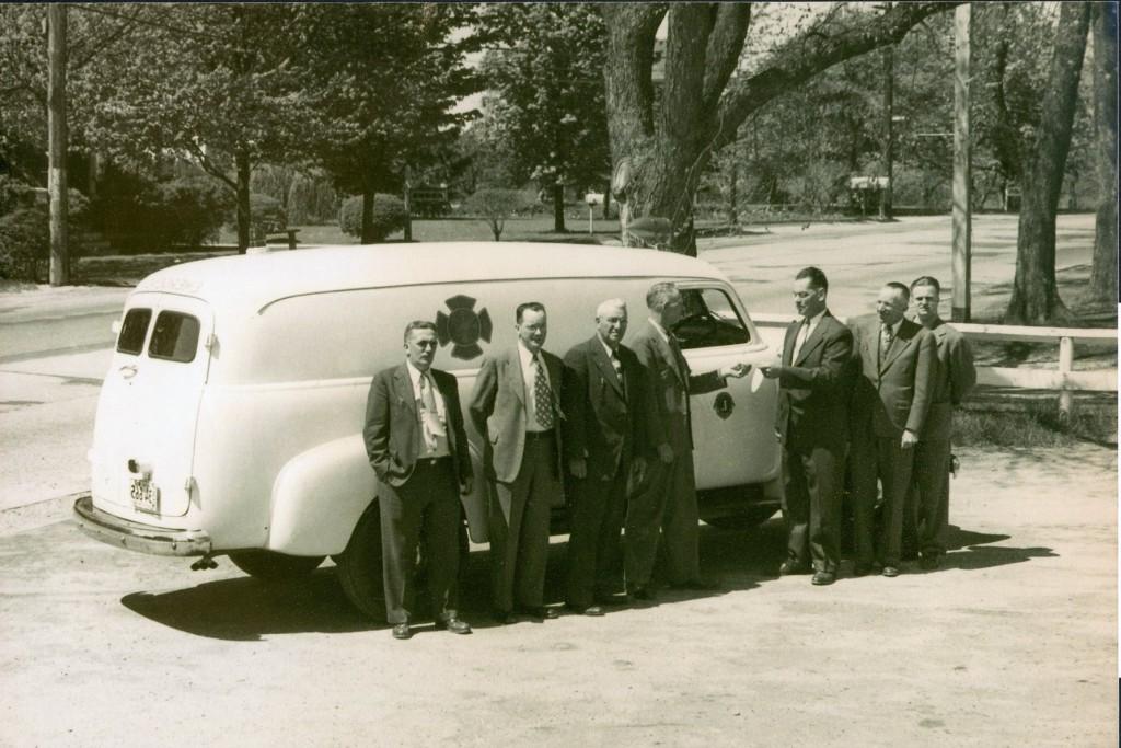 一辆白色救护车的历史照片，前面站着几个人