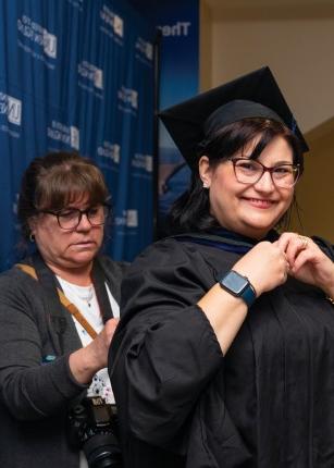 A faculty member help a student put on their gown at commencement