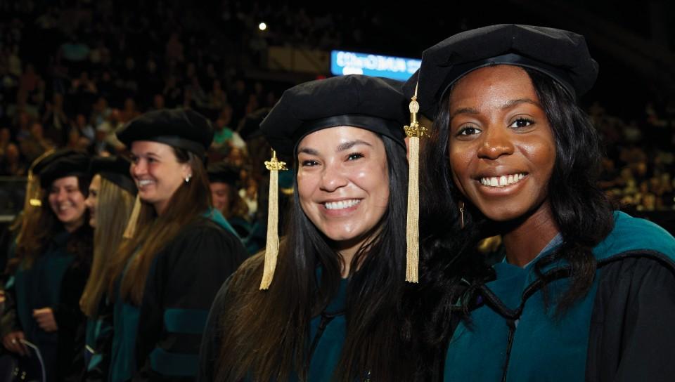 Two graduating students smile for the camera during the 2023 U N E commencement ceremony