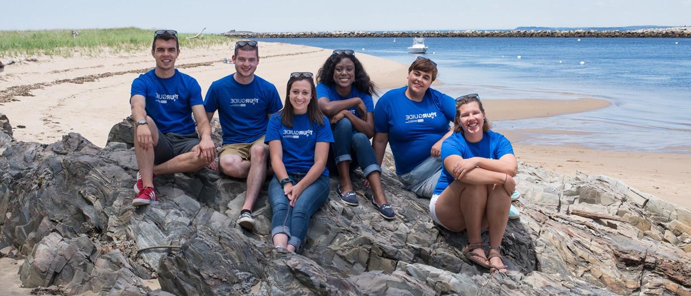 一群英国东北大学的学生导游穿着相配的蓝色衬衫坐在岩石沙滩上