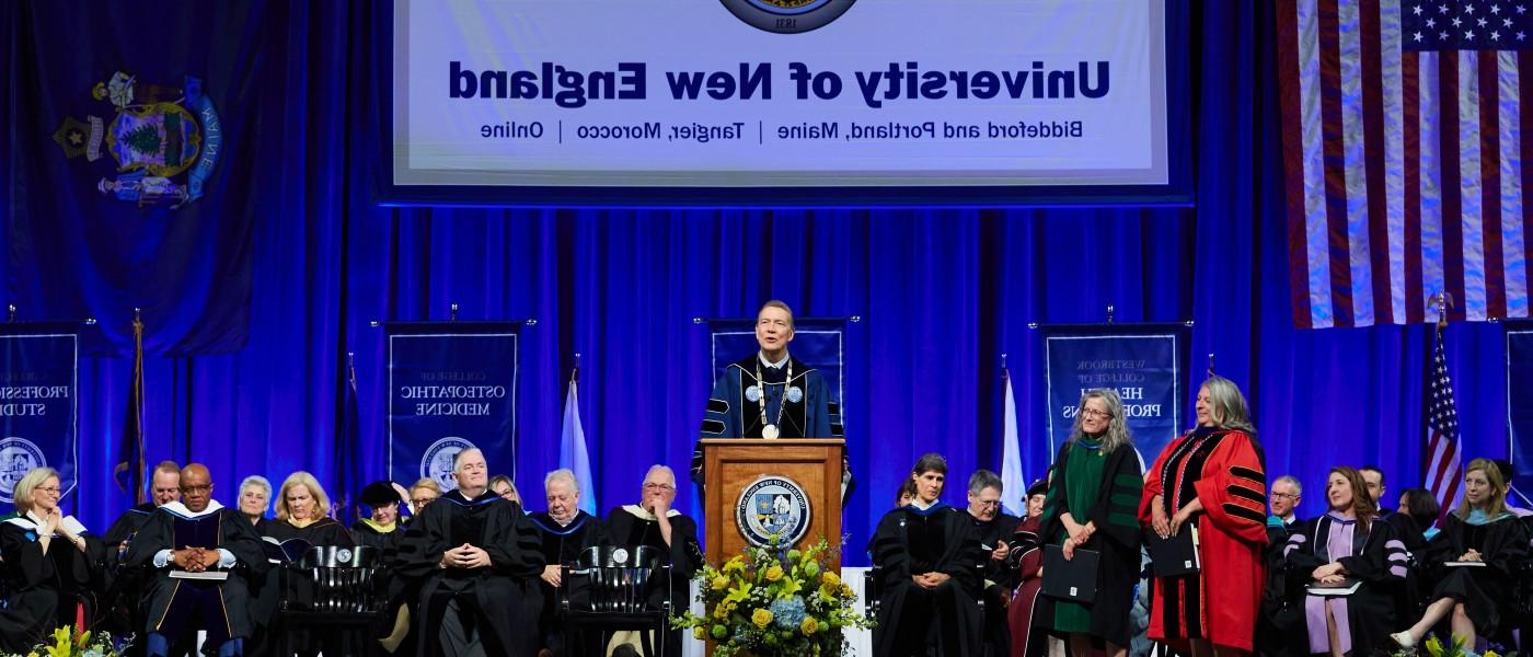 U N E President james herbert stands at the podium with faculty seated behind him at 2023 commencement