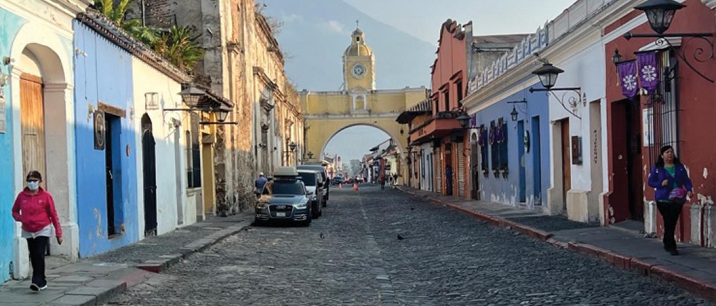 Street view of colorful buildings that lead to a yellow arch with a tower