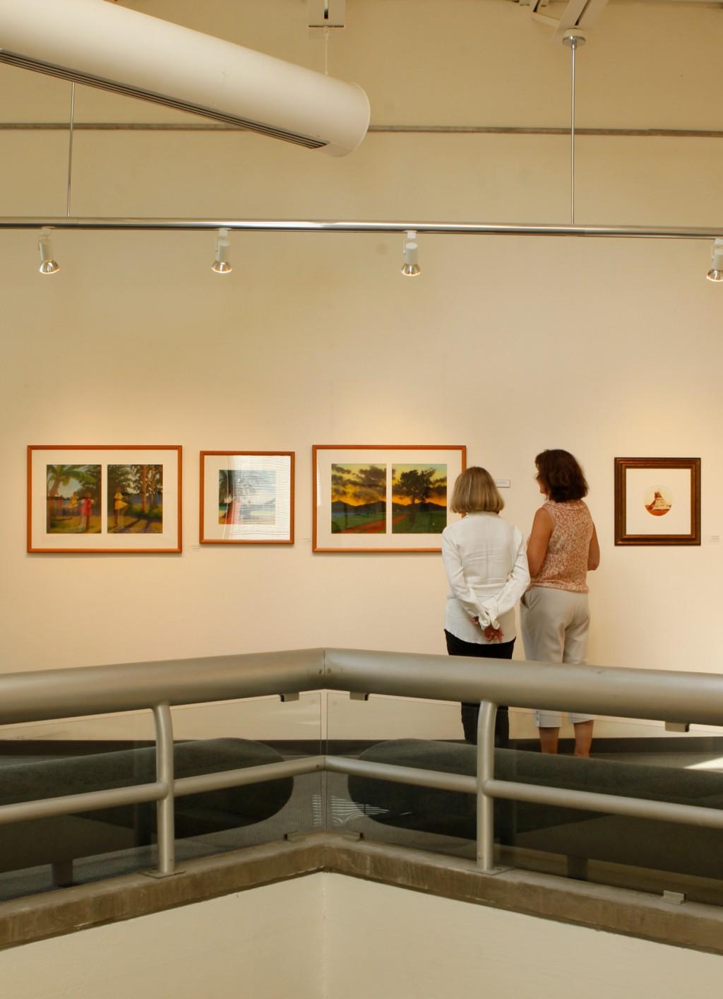 波特兰校园美术馆里，两名妇女在看挂在白墙上的一排装裱好的油画