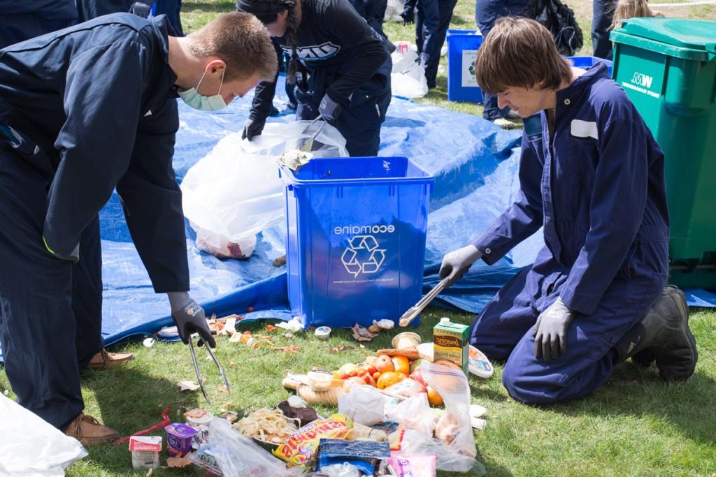 Two students in coveralls are sifting through trash to find items for recycling