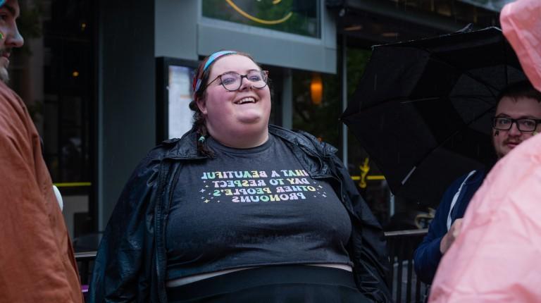 A woman's shirt reads "What a Beautiful Day to Respect Other People's Pronouns"